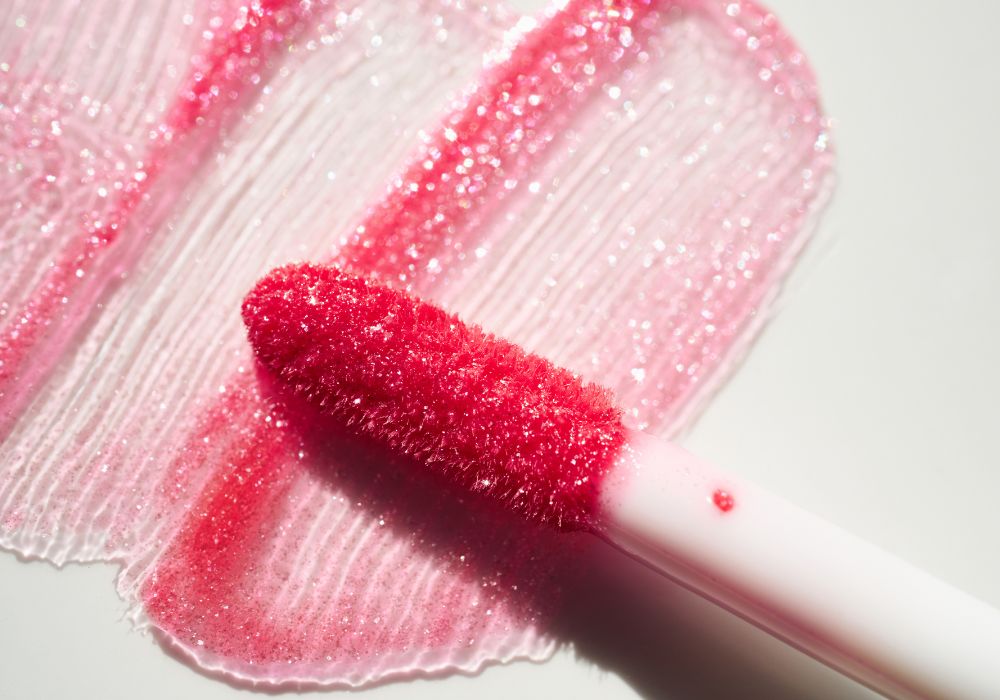 Gros plan sur l’applicateur et la texture brillante d’un gloss rose maison à la framboise.