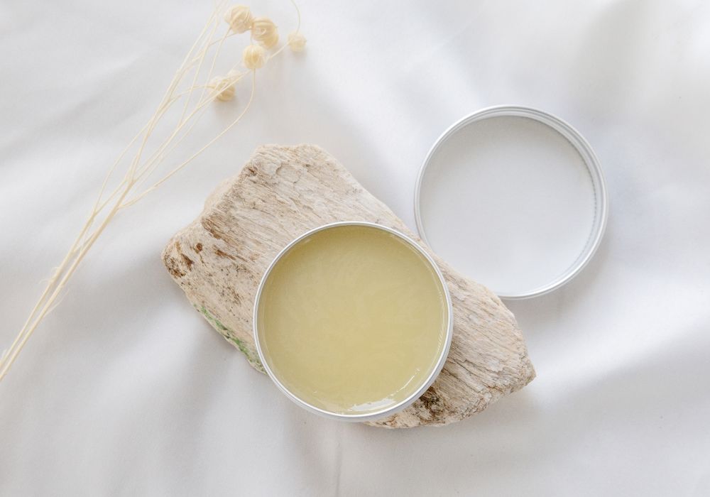 Déodorant solide maison au bicarbonate dans une boîte métallisée, présenté sur un morceau de bois sur fond clair