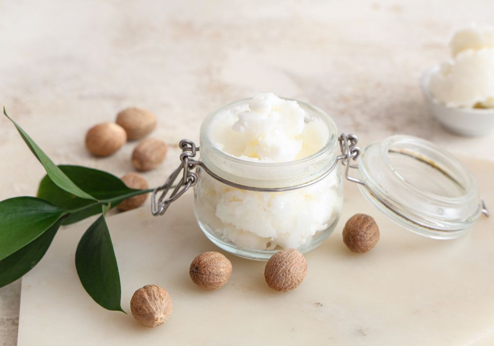 Beurre de karité brut dans un bocal en verre entouré de noix sur une surface claire
