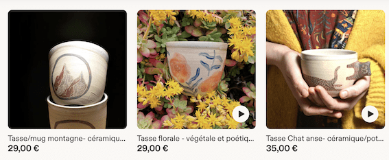 Trois tasses en céramique de Paume de Terre Atelier : une tasse à motif de montagne, une tasse florale posée dans des fleurs jaunes et une tasse à anse en forme de chat tenue dans les mains