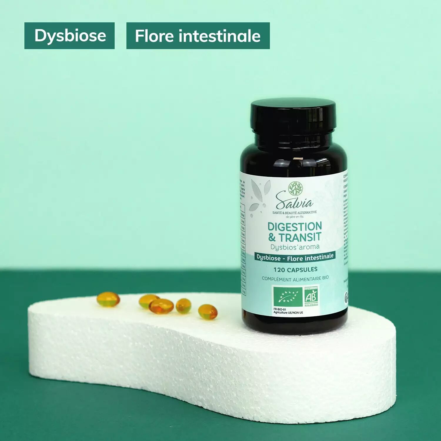 Pot de Dysbios'aroma de Salvia, 120 capsules bio, sur un socle blanc à côté de capsules dorées, sur fond vert, avec les étiquettes de la marque « Dysbiose » et « Flore intestinale »