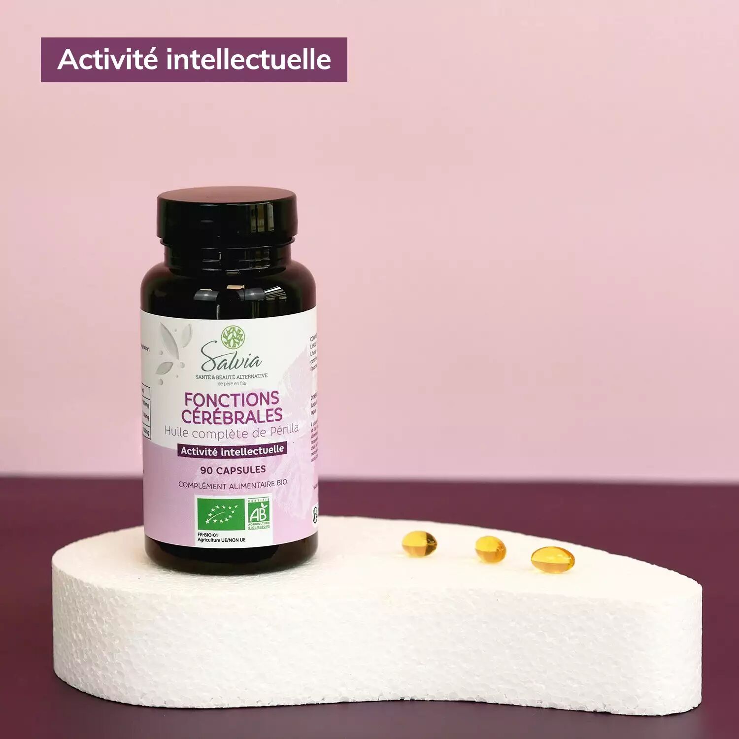 Pot d'huile complète de périlla de Salvia, 90 capsules bio, sur un socle blanc à côté de trois capsules dorées, sur fond rose, avec l'étiquette de la marque « Activité intellectuelle »