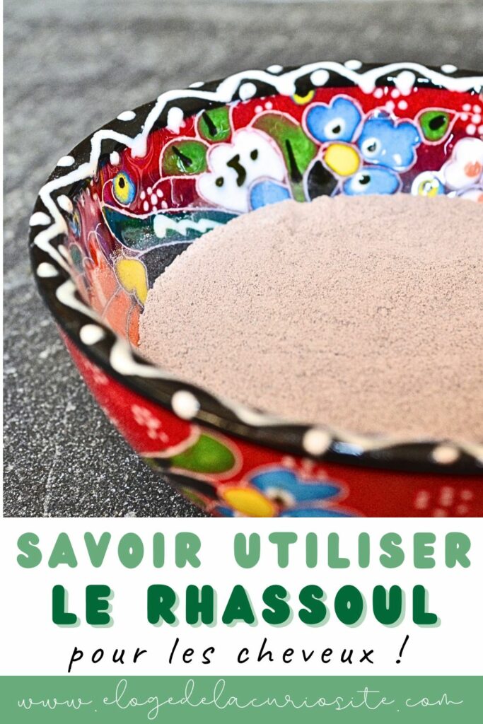 Poudre de rhassoul beige rosé dans un bol en céramique peinte à fleurs rouges et bleues, posé sur un plan de travail gris, avec le texte « Savoir utiliser le rhassoul pour les cheveux !