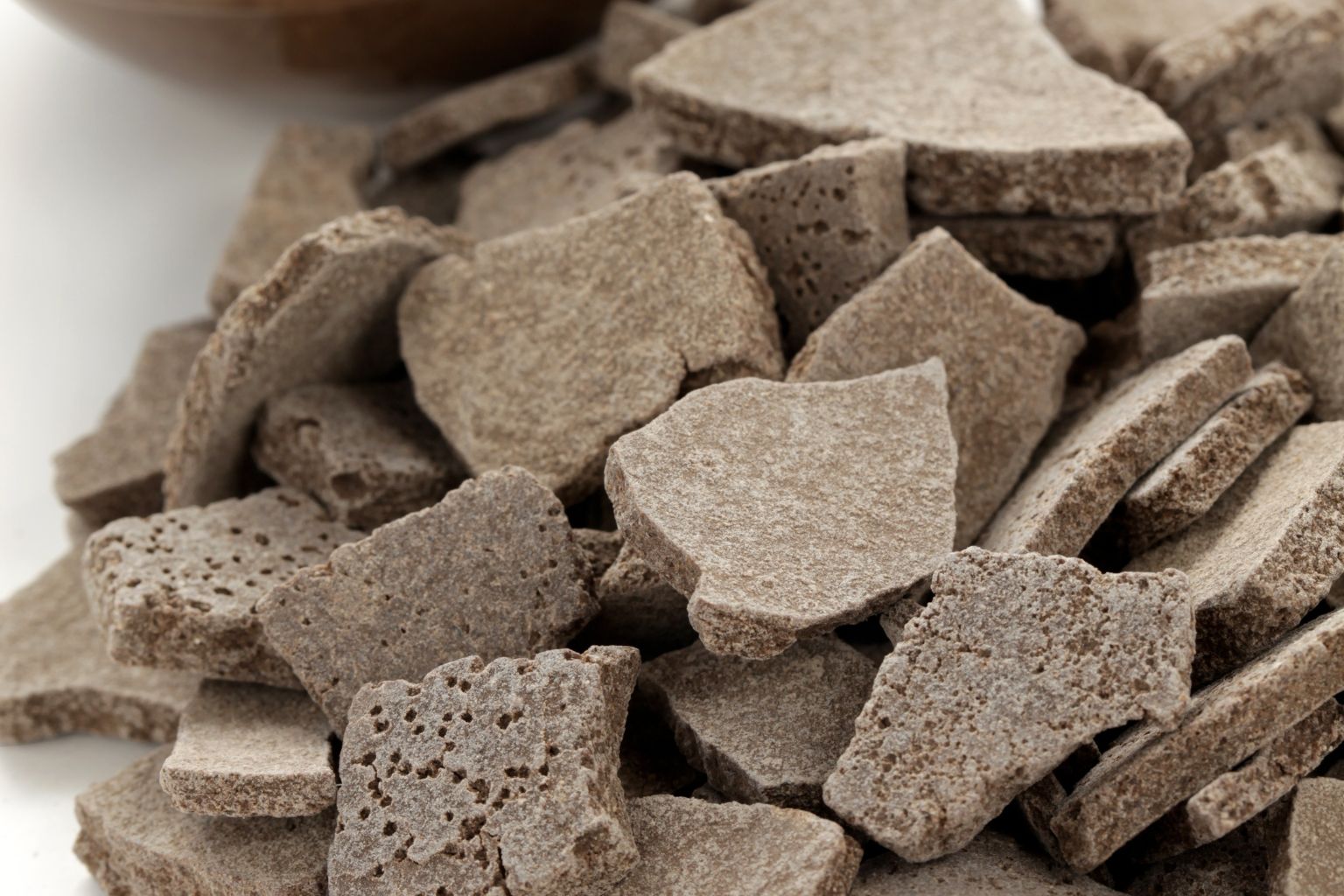Plaquettes brutes de rhassoul brun-gris, à la surface alvéolée, en tas sur un fond blanc